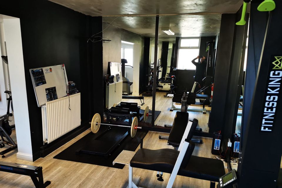 A lifting platform with a loaded barbell, beside a bench and a cable machine, in front of a wall of mirrors.